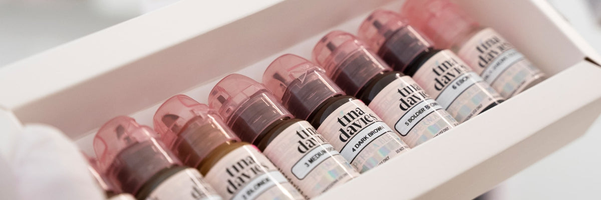 Artist opening the I ❤️ INK Eyebrow Pigment Collection box, showing seven eyebrow pigment bottles inside.