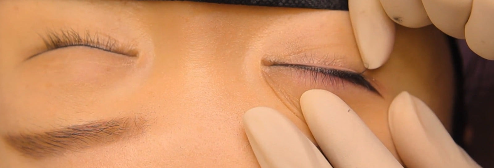 Close-up of a person's eye with a hand applying eyeliner.