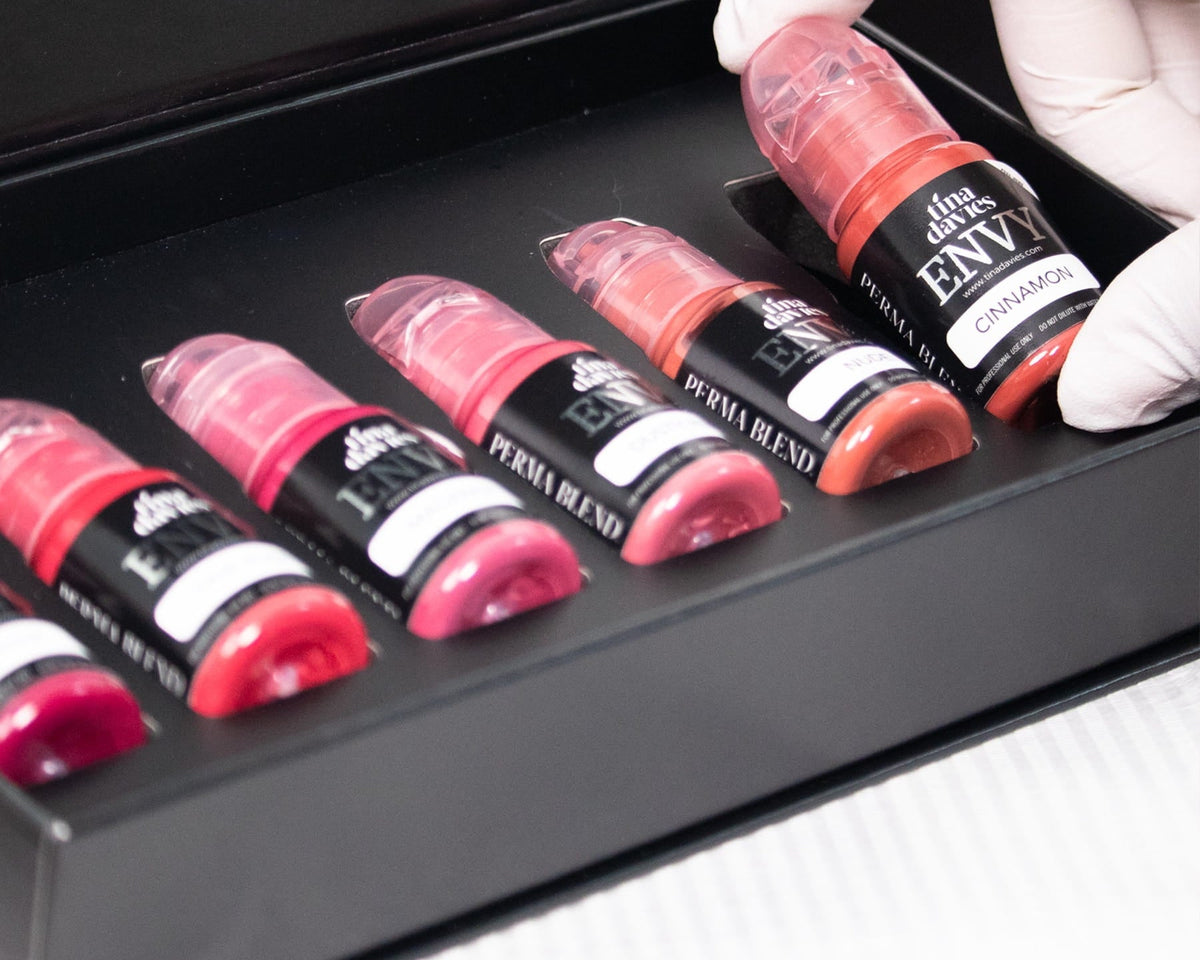 Set of lip glosses in a black tray with a hand wearing a white glove holding one of them.