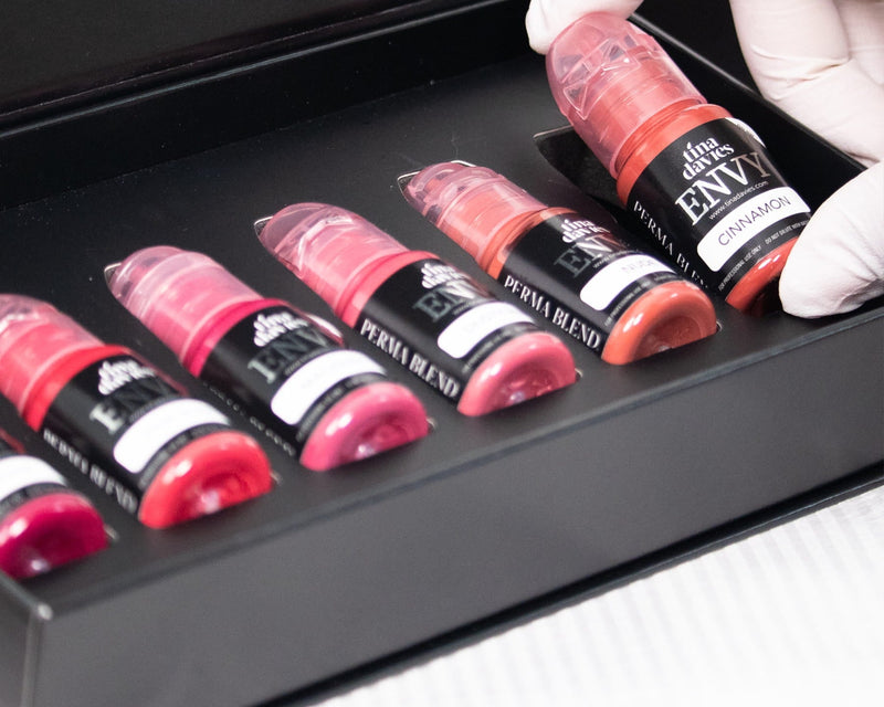 Set of lip glosses in a black tray with a hand wearing a white glove holding one of them.